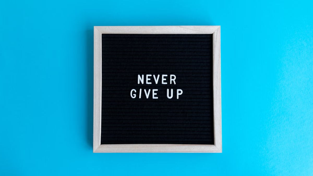 Black letter board with 'Never Give Up' message on a vibrant blue background.